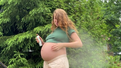 Young pregnant woman suffering of mosquito, insects and using mosquito spray at nature