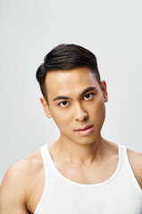Handsome Asian man in a grey tank top confidently posing in a studio setting.