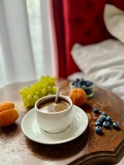 Breakfast in bed. Cup of coffee with fresh fruits on a wooden table in a hotel room.