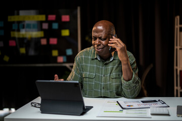 A man is talking on his cell phone while sitting at a desk with a laptop