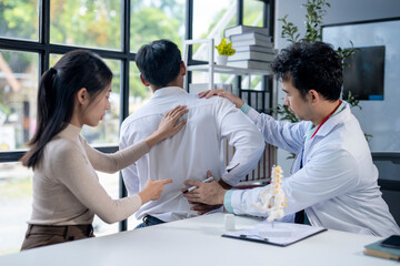 Fototapeta premium A doctor is examining a man's back while a woman looks on
