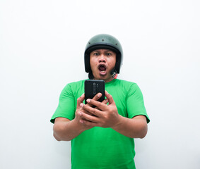 Asian man wearing a helmet and green shirt showing a surprised gesture or expression while holding a mobile phone