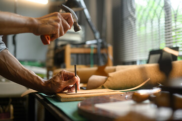 Close up shot craftsman using a hammer and other tools to shape and detail the leather piece
