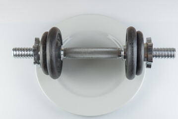 Gym dumbbell in the middle of a pottery plate, on white background. Concept useful for nutrition, fit, digestion, indigest.