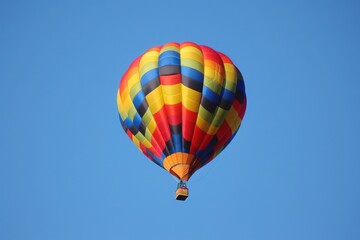 Fototapeta premium Colorful hot air balloon rises gracefully against a clear blue sky, fully inflated and ready for a peaceful and adventurous journey