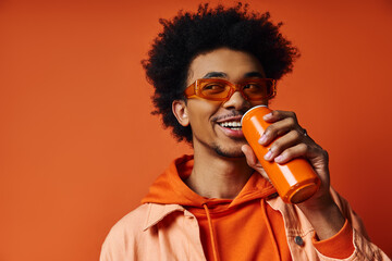 A stylish curly African American man in an orange hoodie holds an orange bottle against an orange...