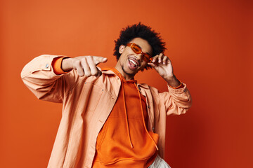 A stylish young African American man with curly hair wearing an orange shirt and sunglasses, posing...