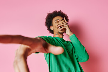A cheerful young African American man in a green shirt smiling on a pink background.