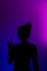 Dark profile of mysterious girl drinking from a glass on colored background.
