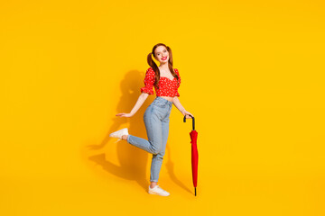 Full body length photo of young lady in red blouse and jeans holding umbrella rainy weather spring season isolated on yellow color background