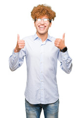 Young handsome business man with afro wearing glasses success sign doing positive gesture with hand, thumbs up smiling and happy. Looking at the camera with cheerful expression, winner gesture.