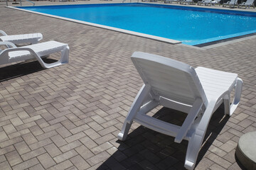 Swimming pool with blue water near the residential complex. White sun loungers, no people. Modern tourism