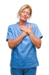 Middle age blonde woman wearing doctor nurse uniform over isolated background smiling with hands on chest with closed eyes and grateful gesture on face. Health concept.