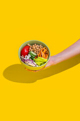 Woman hand holding bowl with salad over isolated yellow background.