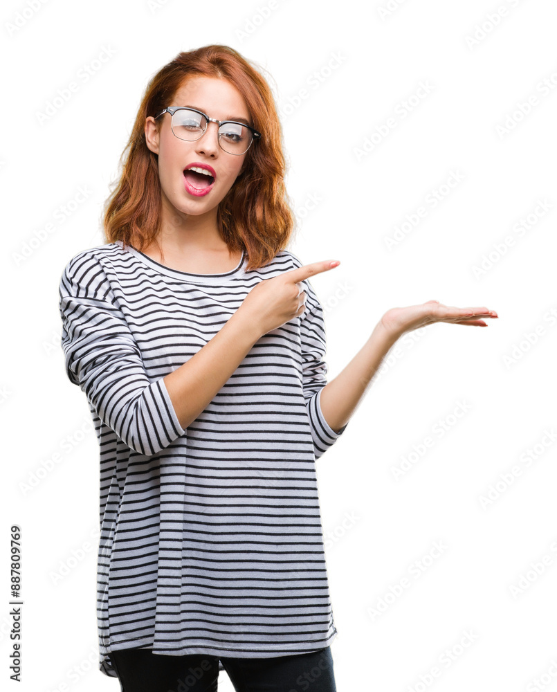 Poster Young beautiful woman over isolated background wearing glasses amazed and smiling to the camera while presenting with hand and pointing with finger.