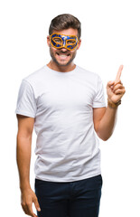 Young handsome man wearing carnival mask over isolated background with a big smile on face, pointing with hand and finger to the side looking at the camera.