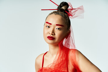 An attractive Asian woman with vibrant red makeup and a veil on her head poses gracefully.