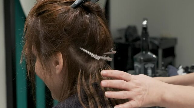 Hairdresser does fusion hair extension by installation natural hairs with heating tool to the client in the salon, Hair extension with keratin, increase hair volume. Professional hair care