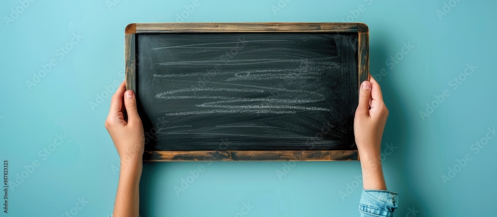Poster Hand holding a blank chalkboard against a blue backdrop with space for text or images. with copy space image. Place for adding text or design