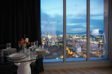 Romantic dining table setting next to window with night city view in a luxury apartment hotel room
