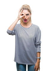 Young beautiful blonde woman wearing stripes sweater over isolated background doing ok gesture shocked with surprised face, eye looking through fingers. Unbelieving expression.