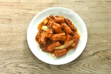 fried pork sausage with slice onion in sweet and sour sauce on plate