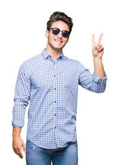 Young handsome man wearing sunglasses over isolated background smiling with happy face winking at the camera doing victory sign. Number two.