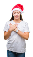 Young beautiful caucasian woman wearing christmas hat over isolated background smiling with hands on chest with closed eyes and grateful gesture on face. Health concept.