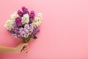 Young adult woman hand holding fresh beautiful bouquet of colorful lilac flowers on light pink wall background. Pastel color. Closeup. Front view. Empty place for text.