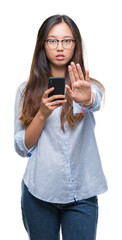 Young asian woman texting using smartphone over isolated background with open hand doing stop sign with serious and confident expression, defense gesture