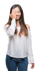 Young asian woman over isolated background covering one eye with hand with confident smile on face and surprise emotion.
