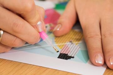 A close-up of a hand placing crystals on a canvas for a diamond painting project. Diamond Mosaic