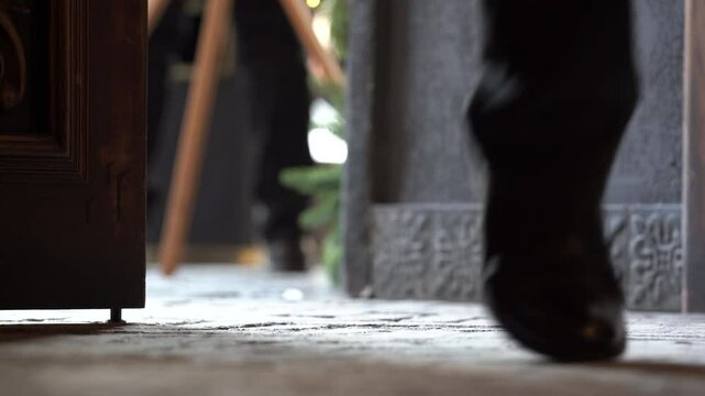  Person's leg enter to room. Peron in black shoes enter to room. Man open wood door and enter.