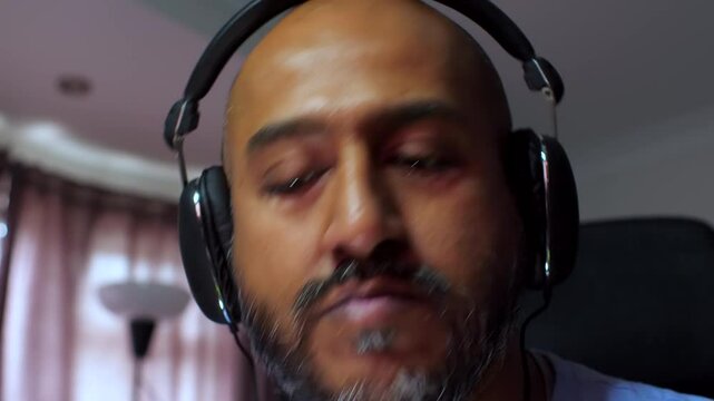 Close-up of a South Asian male working from home, wearing a headset, listening to music, and bopping his head. Relaxed and focused atmosphere.