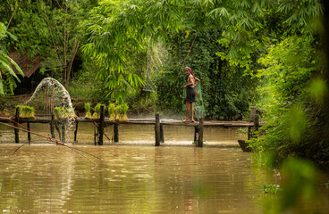 Fisherman atop the bridge netting fish in the river with a fishnet