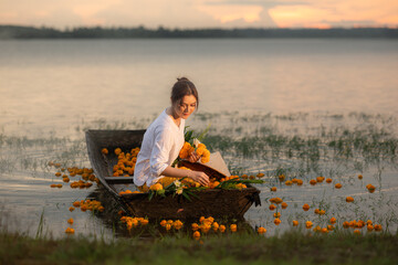 Young woman on a boat with yellow flowers in the lake during the sunset © Wosunan