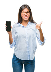 Young asian woman showing smartphone blank screen over isolated background happy with big smile doing ok sign, thumb up with fingers, excellent sign