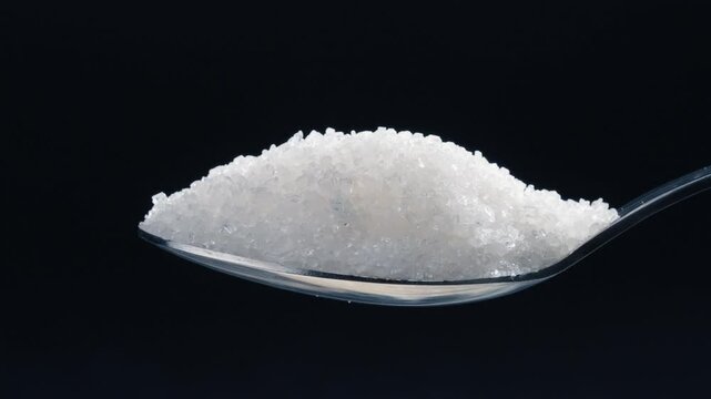 close-up on a black-blue background white crumbly granulated sugar lies on it crystal sugar spills from a spoon harmful to health