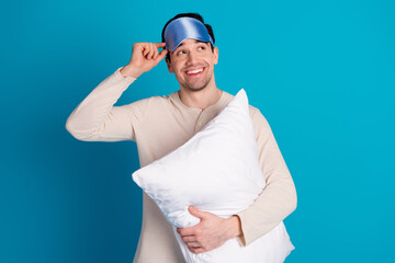 Portrait of nice young man cushion look empty space wear pajama isolated on blue color background