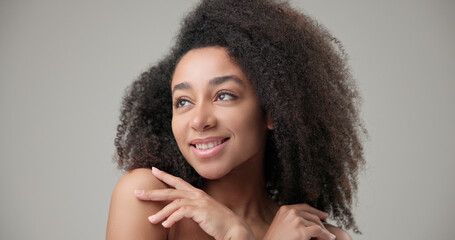 Beauty and healthcare concept - beautiful African American woman with curly afro hairstyle and clean, healthy skin touching face with hand, doing facial massage, posing and looking at camera