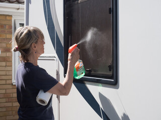 A lady motorhome owner cleans her recreational vehicle windows with green liquid spray gun.RV.