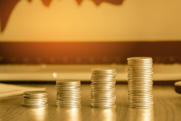 Stack of money coin on wood desk with laptop computer open trading graph in the background, Business and Financial concept. 
