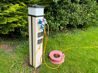 Electric hook-up cables have been plugged into a campsite electrical supply point.An extension lead can be seen on the ground.Hook Up.Motorhoming.