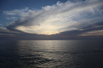 Obraz premium Sunset on the sea, sun behind the cloud, cloudy landscape