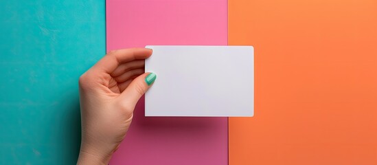 Fototapeta premium A female hand displaying a blank business card against a colorful background allowing for copy space image