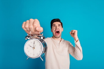 Portrait of nice young man hold alarm shout raise fist wear pajama isolated on blue color background