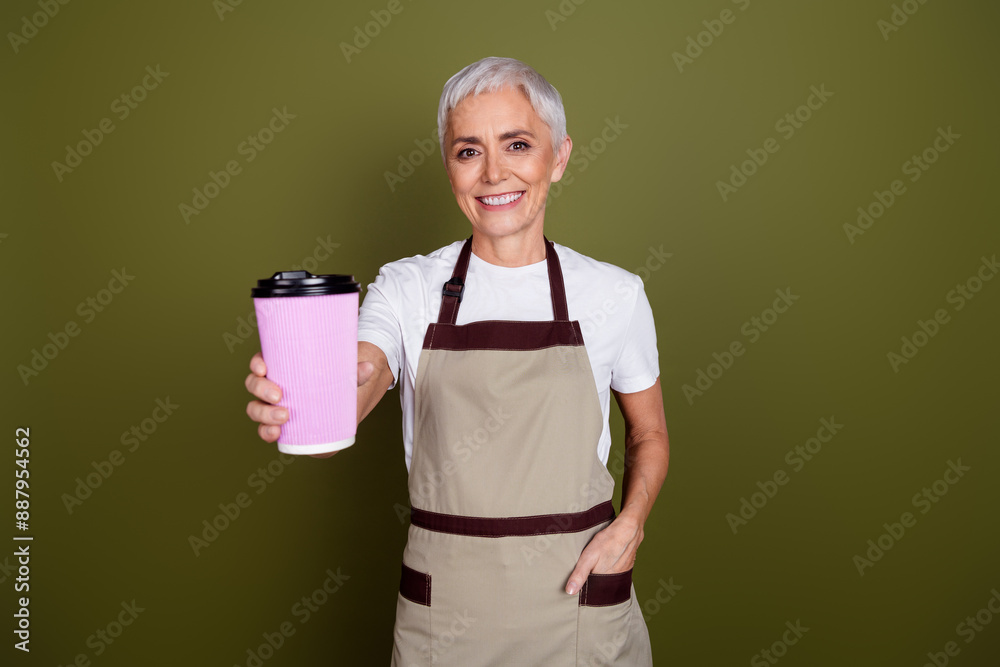 Sticker Photo of smiling positive woman wear apron serving you coffee to go empty space isolated khaki color background