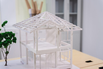 Desk of an engineer displays a concrete house structure under construction. A toy house model sits...