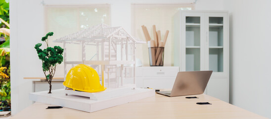 Desk of an engineer displays a concrete house structure under construction. A toy house model sits...
