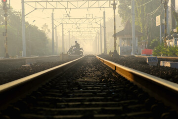 A man riding a motorbike across train tracks in the morning; shrouded in fog